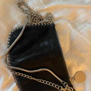 Svart axelväska med kedjedetaljer - Snygg svart axelväska med glittrig yta och kedjedetaljer. Passar till så många tillfällen !💕