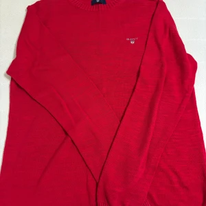 Röd tröja från Gant - Snygg röd tröja från Gant med rund hals och diskret logga på bröstet. Perfekt för en stilren look. Tröjan har långa ärmar och är tillverkad i ett mjukt material.