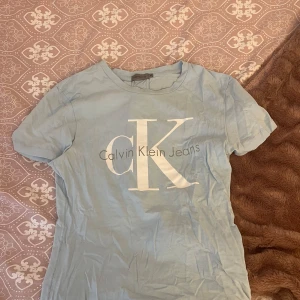 Ljusblå t-shirt från Calvin Klein Jeans - Säljer en ljusblå t-shirt från Calvin Klein Jeans med det ikoniska CK-logotypen tryckt på framsidan. T-shirten har en klassisk rund hals och korta ärmar. Perfekt för en avslappnad stil. Helt oanvänd i storlek xs