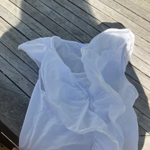 Vit blus med volang - Säljer en söt vit blus med stor volang framtill. Perfekt för dig som gillar romantiska detaljer och vill ha något luftigt och stilrent. Blusen har korta ärmar och är tillverkad i ett lätt material.
