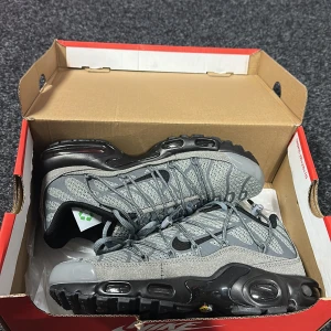 Grå Nike Air Max sneakers - Säljer ett par grå Nike Air Max sneakers med svarta detaljer och synlig luftdämpning i sulan. Skorna har snörning och en sportig design med mesh och syntetmaterial. 