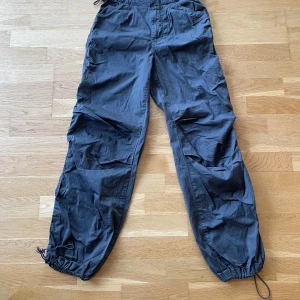 Mörk gröna parachute byxor - Säljer ett par mörk gröna parachute byxor med justerbar dragsko vid bensluten och i midjan . Byxorna har bakfickor som ej går att öppna. Perfekta för en casual look.