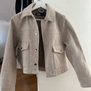 Beige kappa - Säljer denna söta beige kappan. Kappan är i nyskick och har knappt används. Den har en klassisk krage, stora fickor med lock och silverfärgade knappar framtill. Materialet känns mjukt och lite ulligt, perfekt för nu inför våren💕