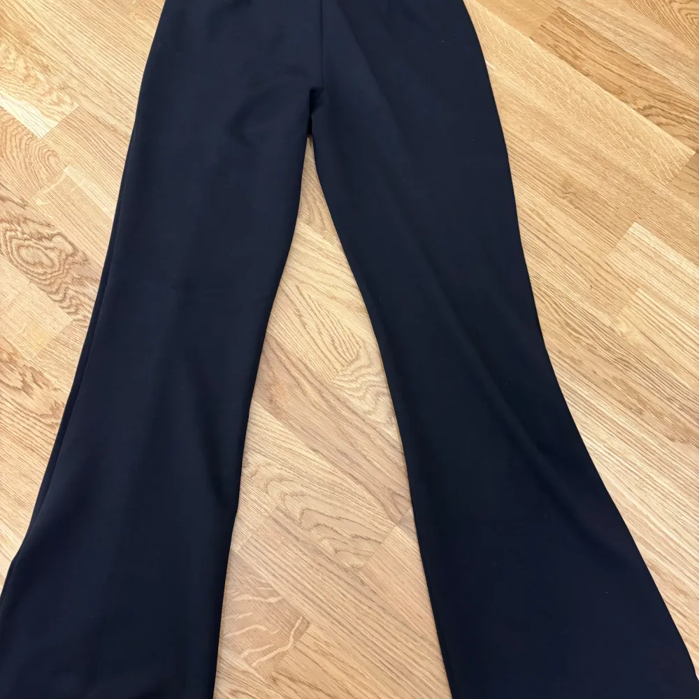 Snygga svarta byxor från Vila med utsvängda ben och hög midja. Perfekta för dig som gillar en stilren look med lite extra attityd. Byxorna har en klassisk passform och är tillverkade i ett mjukt material som sitter skönt hela dagen.. Farkut & Housut.