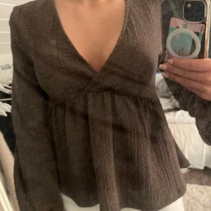 Brun långärmad blus från Gina Tricot - Säljer en brun långärmad blus från Gina Tricot i storlek XXS. Blusen har v-ringning, struktur i tyget och volangig ärm. 