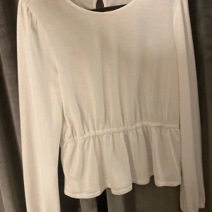 Vit långärmad topp med rynk i midjan - Säljer en vit långärmad topp med rund halsringning och rynkdetalj i midjan som ger en fin form. Den är ifrån ABOUT YOU nästan aldrig använd.