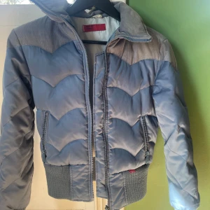 Blå quiltad jacka från Levi's - Säljer en cool blå quiltad jacka från Levi's Red Tab. Jackan har en unik vågig quiltning och dragkedja framtill. Den har långa ärmar och ribbade muddar vid ärmslut och nederkant. Perfekt för kyliga dagar!