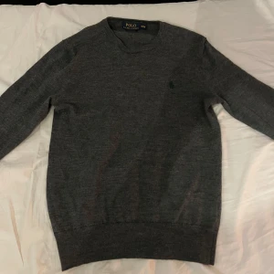 Polo Ralph Lauren stickad tröja - Säljer en stilren grå tröja från Polo Ralph Lauren. Tröjan är långärmad och har en   broderad logga på bröstet. Perfekt för en klassisk och avslappnad look. Storlek M men känns som S