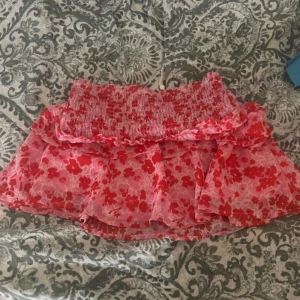 Rosa blommig kortkjol från ONLY - Supersöt kortkjol från ONLY i rosa och rött med blommigt mönster. Kjolen har volanger och bred smock i midjan för en bekväm passform. Perfekt för dig som gillar färg och mönster! Den är i storlek 158cm/13år men är själv 14 år och 163 och skulle säga att den passar ännu längre och äldre ungdomar.