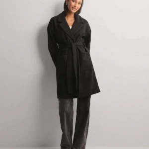 Svart kappa med bälte - Säljer en svart kappa med klassisk krage och knytbälte i midjan. Jackan har långa ärmar och två stora fickor framtill. Varsamt använd🫶🏻