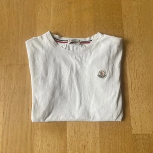 Vit t-shirt från Moncler - Snygg vit t-shirt från Moncler med klassisk rund hals och broderad Moncler-logga på bröstet. T-shirten har en enkel och stilren design med diskreta ränder på insidan av kragen. Storleken står inte men Tor att den passar 160-170. Skriv privat för mer info.