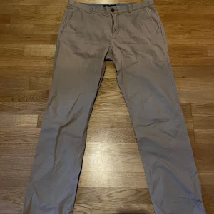 Beige chinos från Tommy Hilfiger - Säljer ett par klassiska beige chinos från Tommy Hilfiger. Byxorna har normal passform, dragkedja och knapp framtill samt fickor både fram och bak. Perfekta för en stilren och avslappnad look.