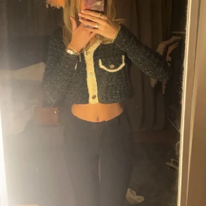 Svart glittrig kofta med vita detaljer - Snygg svart glittrig kofta med vita kanter och dekorativa knappar. Den är croppad och har långa ärmar, perfekt för att ge en stilren touch till din outfit. Passar fint till en kjol🩷 köp för 250kr aldrig använd, bara tvättad men säljer pga flytt