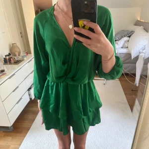 Grön omlottklänning med volang - Säljer en snygg grön kortklänning från Zara med omlott-detalj och volang i kjolen. Klänningen har långa ärmar och djup v-ringning. Perfekt för dig som vill sticka ut med en färgstark look. 