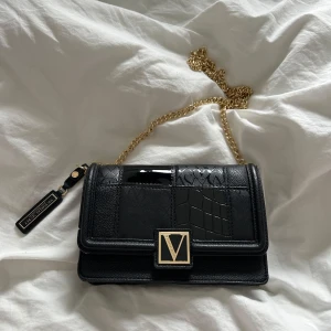 Victoria’s Secret  - Elegant svart axelväska med guldkedja och dekorativt V-spänne från Victoria’s secret. Helt oanvänd 
