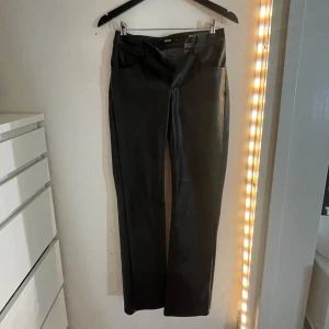 Svarta lågmidjade byxor i skinnimitation från BikBok - Snygga svarta byxor i skinnimitation från BikBok. De har en rak passform och hög midja med dragkedja fram. Perfekta för en trendig look.