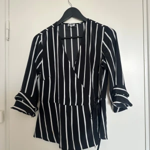 Omlottblus - Svart-vit randig omlottblus med trekvartsärmar och knytband. Stl 40 men sitter som S!