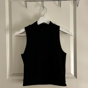 Svart ärmlös topp - Snygg svart ärmlös topp med hög hals. Perfekt för lager-på-lager eller att bära som den är. Enkel och stilren design som passar till många olika outfits.