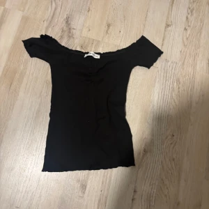 Svart offshoulder topp från New yorker  - Snygg svart offshoulder topp från Sisters Point. Den har en ribbad struktur och korta ärmar, perfekt för en stilren look. Passar bra till både jeans och kjol.