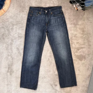 Levi’s 514 - Säljer ett par klassiska blå jeansbyxor med en straight passform. Byxorna har en knapp och dragkedja framtill samt fem fickor. Perfekta för en avslappnad stil. Original längden har blivit klippt och har nu en längd på 65 cm.