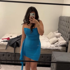 Blå axelbandslös klänning - Snygg blå axelbandslös klänning med asymmetrisk design och draperad detalj på sidan. Perfekt för en kväll ute eller en speciell tillställning.