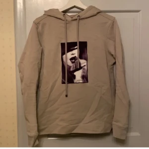 Limitato hoodie  - Säljer en beige hoodie med ett unikt tryck på framsidan. Tröjan har långa ärmar och en klassisk huva med dragsko. Perfekt för en avslappnad stil.