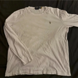 Vit långärmad tröja från Ralph Lauren - Säljer en stilren vit långärmad tröja från Ralph Lauren med det klassiska logotypbroderiet på bröstet. Tröjan har en rund halsringning och är i en slim fit-modell. Perfekt för en avslappnad men ändå elegant look.