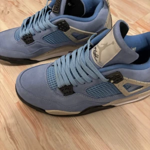 Jordan 4 - Snygga blå Nike Air Jordans med svart och grå detaljer. Skorna har snörning och en ikonisk Jumpman-logga på sulan. Perfekta för dig som vill ha en stilren och sportig look.