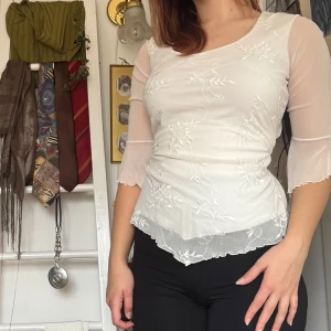 Vit blus med broderade detaljer - Köpt secondhand och använt en del. Säljer en elegant vit blus med broderade blommönster och trekvartsärmar. Blusen har en knytning i ryggen och en lätt transparent design som ger en romantisk känsla. Perfekt för att lyfta vilken outfit som helst!