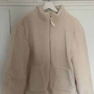 Beige teddyjacka med dragkedja - Mysig beige teddyjacka med dragkedja framtill. Jackan har en hög krage och två stora fickor.  Säljer då den är för stor för mig, därmed aldrig använd.