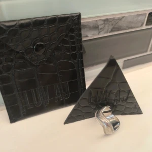 Silverfärgad ring från LUV AJ - Stilren och modern silverfärgad ring från LUV AJ med en vågig design. Perfekt för att ge en elegant touch till din outfit. Kommer i en snygg förpackning med krokodilmönster.