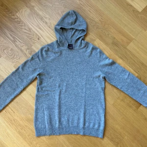 Grå kashmir hoodie från Oscar Jacobson - Säljer en stilren grå hoodie från Oscar Jacobson. Tröjan är tillverkad i Italien och har en klassisk design med långa ärmar och en bekväm huva. Perfekt för en avslappnad look. I Kashmir orginal pris 1700 KR