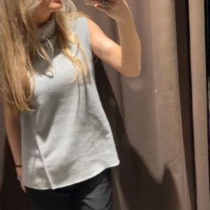 Grå ärmlös polotröja - Säljer en stilren grå ärmlös polotröja i mjukt material. Perfekt för lager-på-lager eller som den är. Tröjan har en hög polokrage som ger en elegant touch. Passar bra till både jeans och kjol.