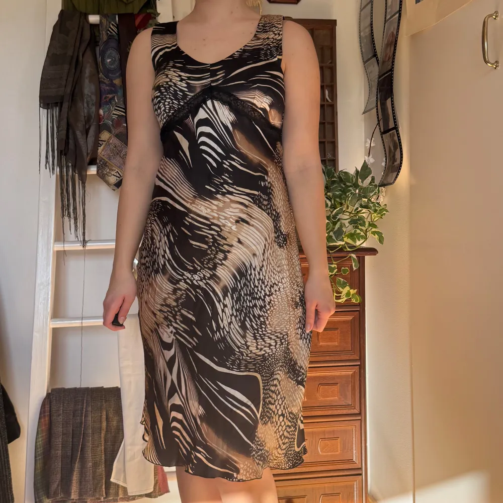 Vintage!! Köpt secondhand och använd några få gånger. Snygg ärmlös klänning med abstrakt mönster i svart och beige. Klänningen har en v-ringad design och är knälång, vilket ger en elegant look. Perfekt för både vardag och speciella tillfällen.. Mekot.