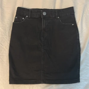 Svart jeanskjol - Snygg svart jeanskjol med klassisk femficksdesign och knappstängning fram. Perfekt för en stilren look.