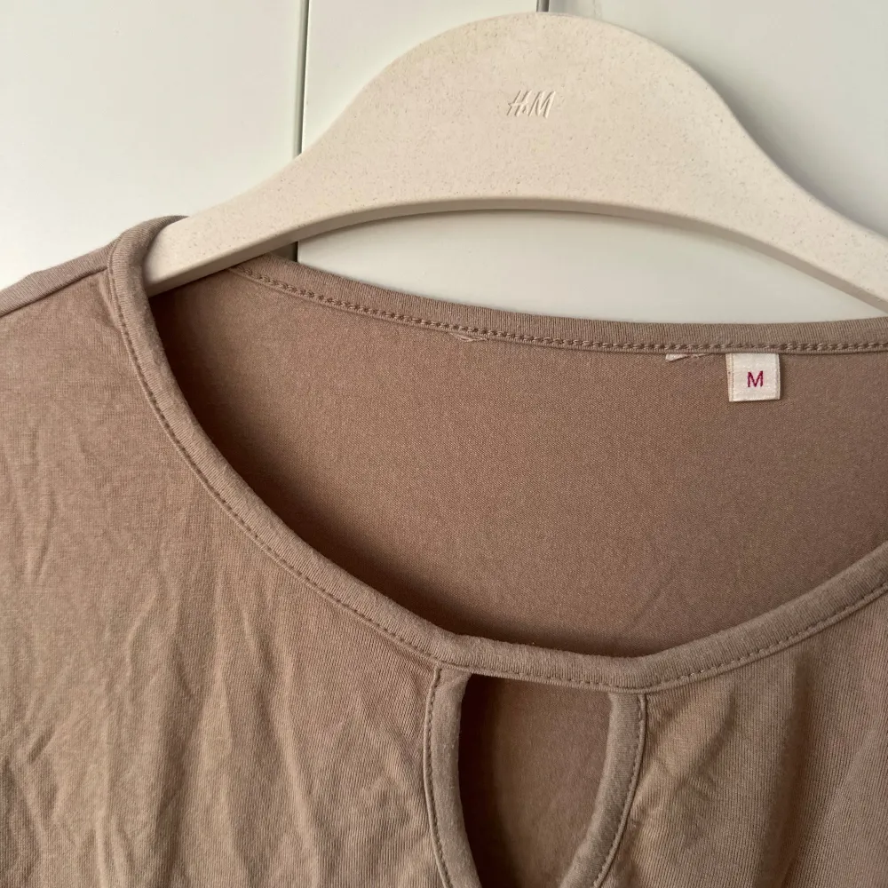 Säljer en stilren beige långärmad topp. Toppen har en rund halsringning med en liten öppning framtill som ger en fin detalj. Perfekt för en avslappnad look. Passar bra till jeans eller kjol.. Neuletakit & Villapaidat.