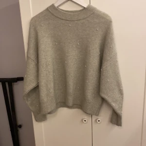 Grå stickad tröja från H&M - Säljer en mysig grå stickad tröja från H&M med pärldetaljer. Tröjan har en normal passform och långa ärmar. Perfekt för kyliga dagar!