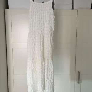 Vit klänning från Zara - Säljer en vit midiklänning från Zara med ett unikt texturerat mönster. Klänningen har smala axelband och en knytning i ryggen för extra detalj. Perfekt för varma dagar! Storleken är som xs