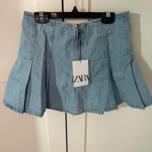 Ljusblå jeanskjol från Zara - Säljer en snygg ljusblå jeanskjol från Zara med dragkedja bak/fram. Man kan ha kjolen på båda hållen. Kjolen har en kort och utsvängd design som ger en trendig look. Perfekt för en avslappnad stil. 🩵storleken är som en xs/s
