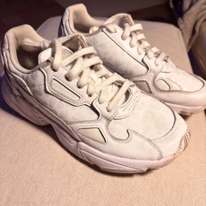 Adidas Falcon Chrystal White - Säljer ett par vita Adidas sneakers med diskret mönster och snörning. Skorna har en chunky sula och Adidas-logga på baksidan. Perfekta för en stilren look.