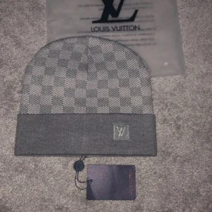 Grå rutig mössa från Louis Vuitton - Snygg grå mössa från Louis Vuitton med ett klassiskt rutigt mönster. Helt ny