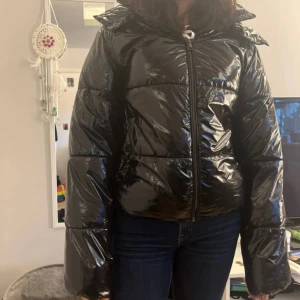 Svart glansig pufferjacka - Säljer en svart glansig pufferjacka ifrån Nelly med dragkedja och huva. Jackan har en quiltad design och långa ärmar, perfekt för kyliga dagar. Den är både stilren och funktionell.Ny pris 450 kr storlek Xs passar dig som är en mindre S