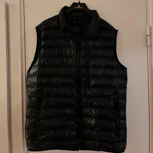 Mörkblå dunväst från Peak Performance - Snygg mörkblå dunväst från Peak Performance med dragkedja framtill. Perfekt för lager-på-lager under kyliga dagar. Västen har en stilren design med diskret logga vid nacken. Köparen står för frakt.