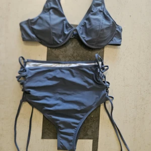 Blå bikini med snörning, stl S - Snygg blå bikini med höga midjetrosor och snörningsdetaljer på sidorna. Överdelen har bygel och breda axelband för extra stöd. Tillverkad i stretchigt material som sitter skönt och formar sig efter kroppen. Perfekt för strandhäng eller poolparty.