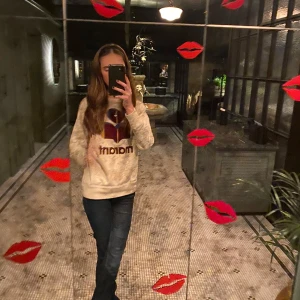 Beige Marant sweatshirt med tryck - Säljer en beige sweatshirt från Isabel Marant med stort lila och rött logotryck framtill. Tröjan har rund hals, långa ärmar och en relaxed passform. Perfekt för dig som gillar streetstyle och vill ha något bekvämt men ändå snyggt.