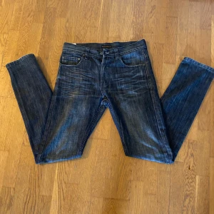 Nudie Jeans Regular Ralf blå jeans - Säljer ett par Nudie Jeans Regular Ralf i klassisk blå tvätt. Jeansen har raka ben, fem fickor och snygga slitningar framtill. Tillverkade i 100% bomull med Nudie-logga på bakfickan och läderpatch i midjan. Perfekta för dig som gillar en tidlös jeanslook.
