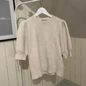 Beige stickad tröja från Vero Moda - Superfin beige stickad tröja från Vero Moda med puffiga trekvartsärmar och ribbade muddar. Perfekt för dig som gillar en enkel men trendig look. Passar till både jeans och kjol för en chill stil. Lite nopprig, blir ju mer man använder den, men superlätt att ta bort med noppborttagare!