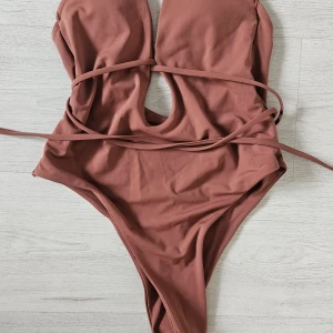 Rost Brun baddräkt med snörning, stl M ftån shein - Snygg brun baddräkt i enkel design med djup v-ringning och smala snören som kan knytas runt midjan. Tillverkad i stretchigt material (80% nylon, 20% spandex) som sitter tight och bekvämt. Perfekt för stranden eller poolen i sommar. 