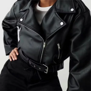 Svart croppad skinnjacka med bälte - Säljer en svart croppad skinnjacka med coola silvriga dragkedjor och bälte i midjan. Perfekt för dig som vill sticka ut och addera lite attityd till din outfit.