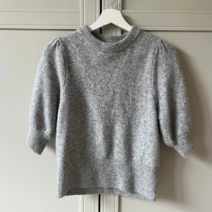 Stickad tröja med puffärm - Grå stickad tröja med korta puffärmar och bred ribbad kant vid hals, ärmslut och nederkant. 